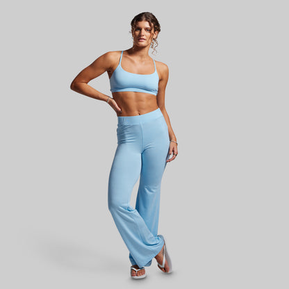 Woman wearing a light blue sports bra and high-waisted wide- leg pants on a gray background