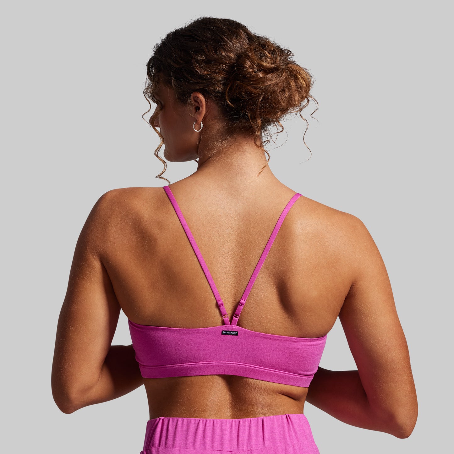 Woman wearing a pink sports bra and shorts on a gray background