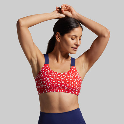 Woman wearing a red sports bra with white star pattern and blue leggings on a gray background