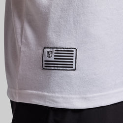 Close-up of a white t-shirt with a black flag patch on a light gray background