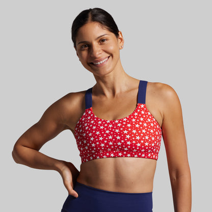 Woman wearing a red sports bra with white star pattern and blue straps on a gray background