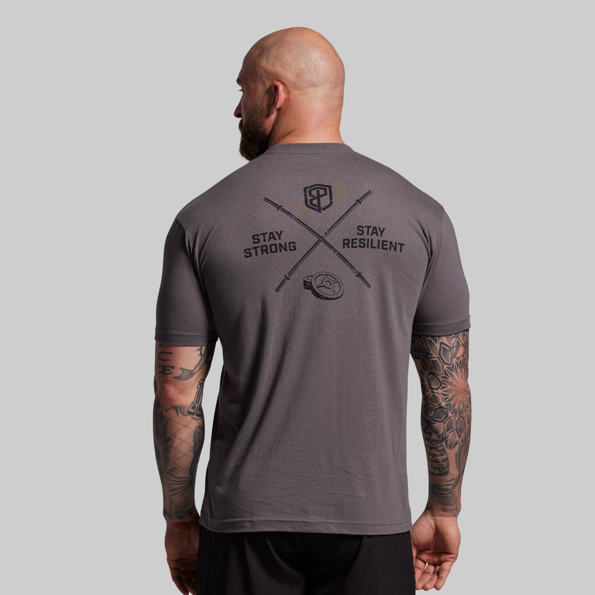 Man wearing a gray t-shirt with motivational text and logo on the back against a plain background