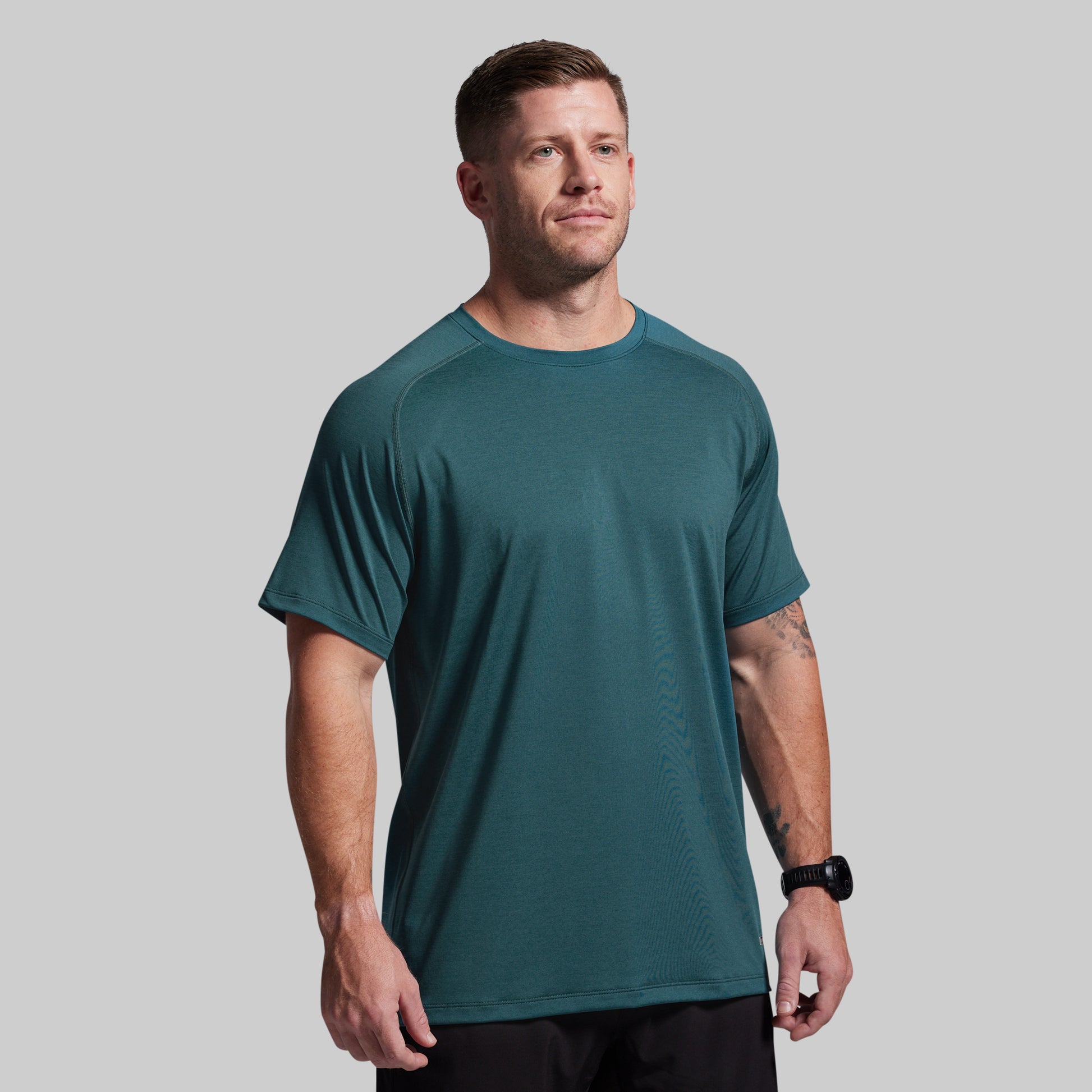 Man wearing a teal athletic shirt on a gray background