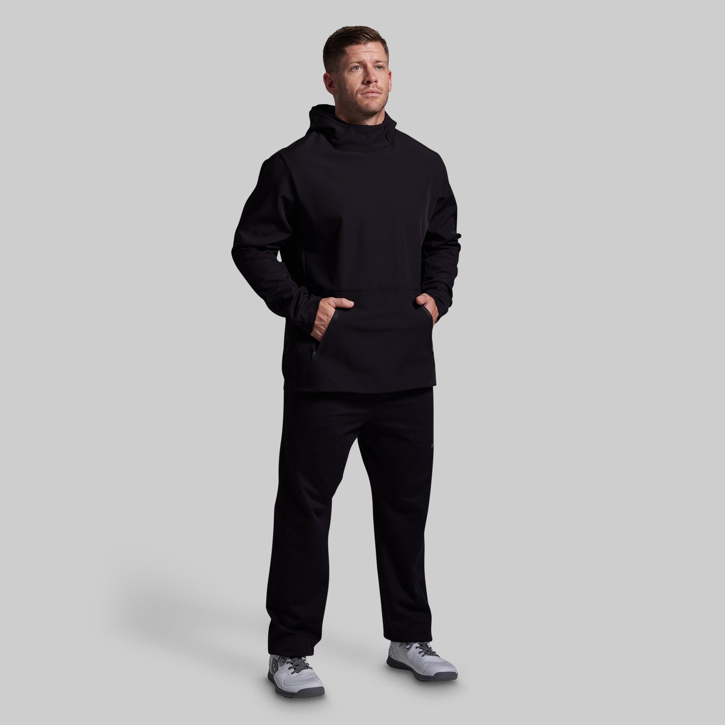 Man wearing a black hoodie and pants on a light gray background