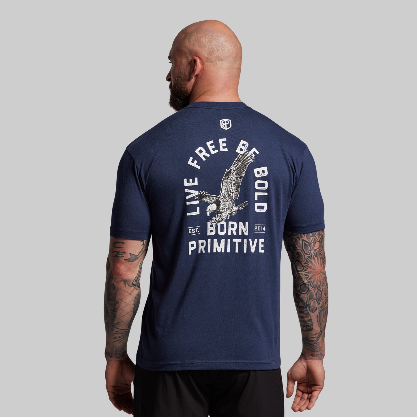 Man wearing a navy blue t-shirt with a design and text on the back, standing against a gray background.