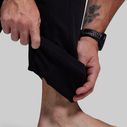 Person showing inside of black athletic pants with a gray background