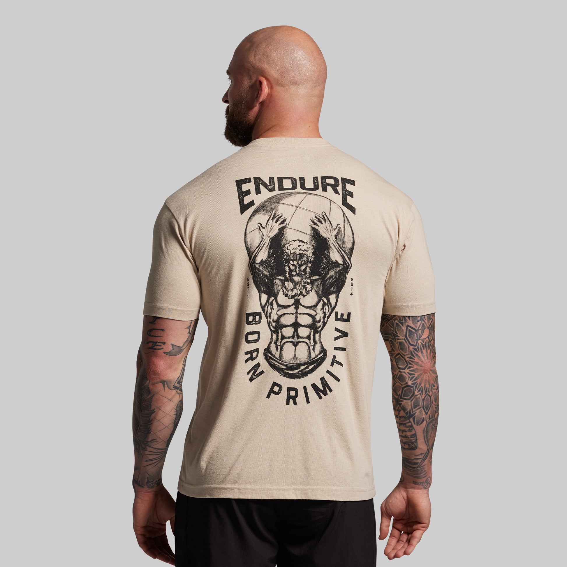 Man wearing a beige t-shirt with 'ENDURE' and graphic design on the back, standing against a gray background.