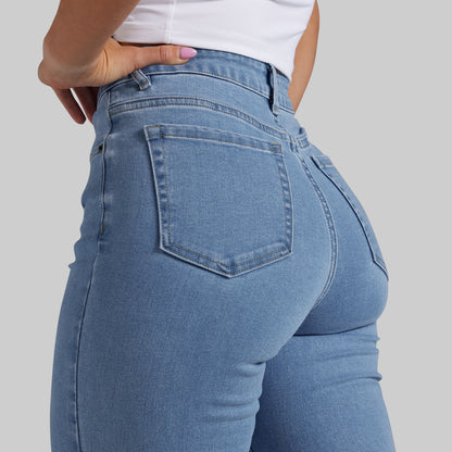 Close-up back view of a person wearing light blue denim jeans with a white top, shown against a plain light gray studio background.