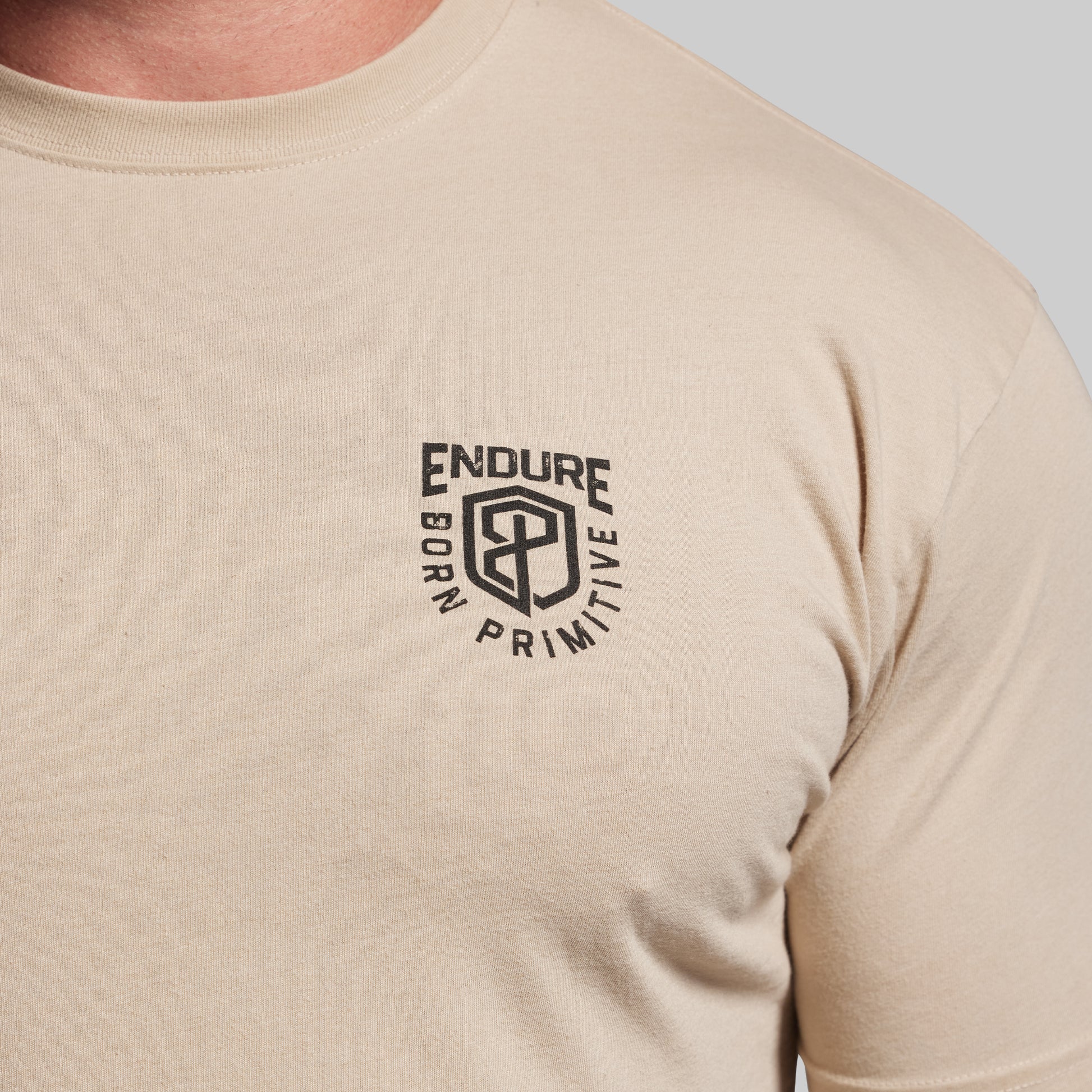 Beige t-shirt with a black logo on a light gray background