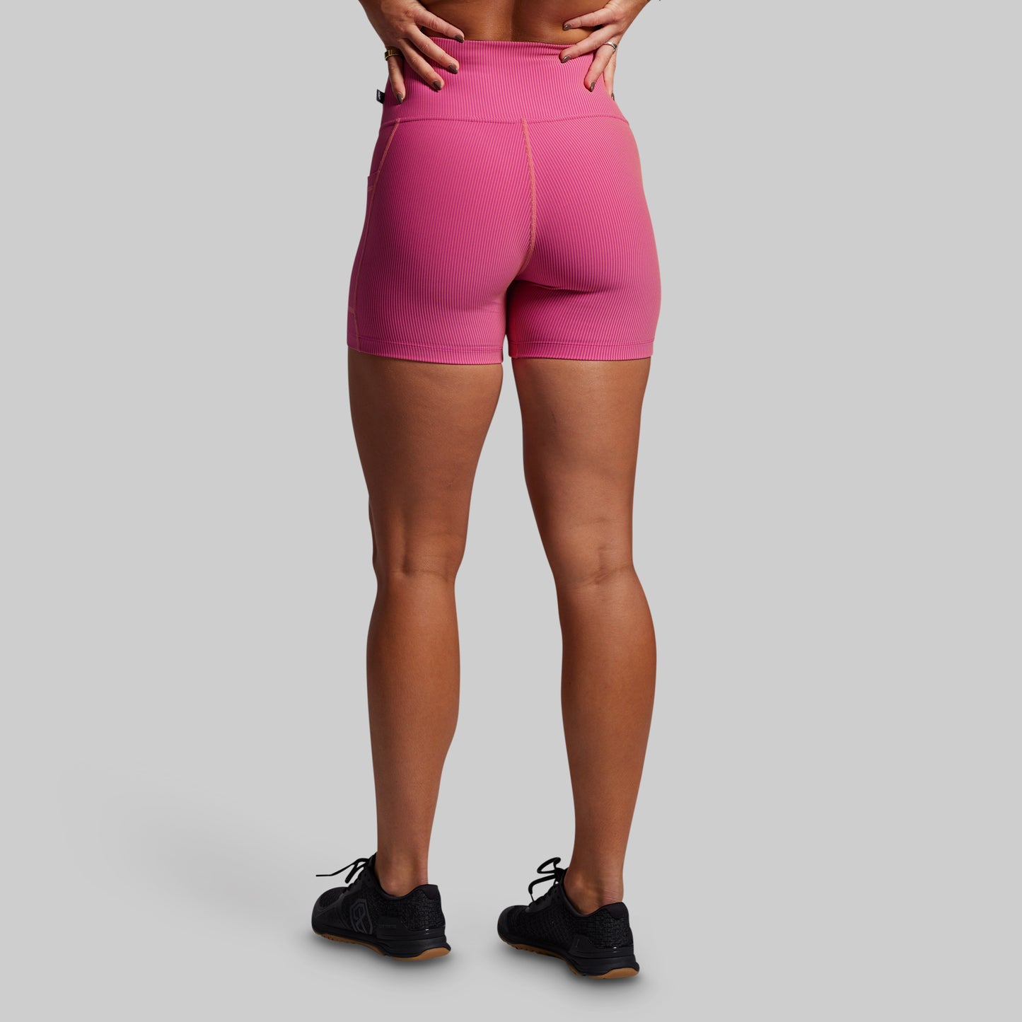 Person wearing pink ribbed athletic shorts on a gray background