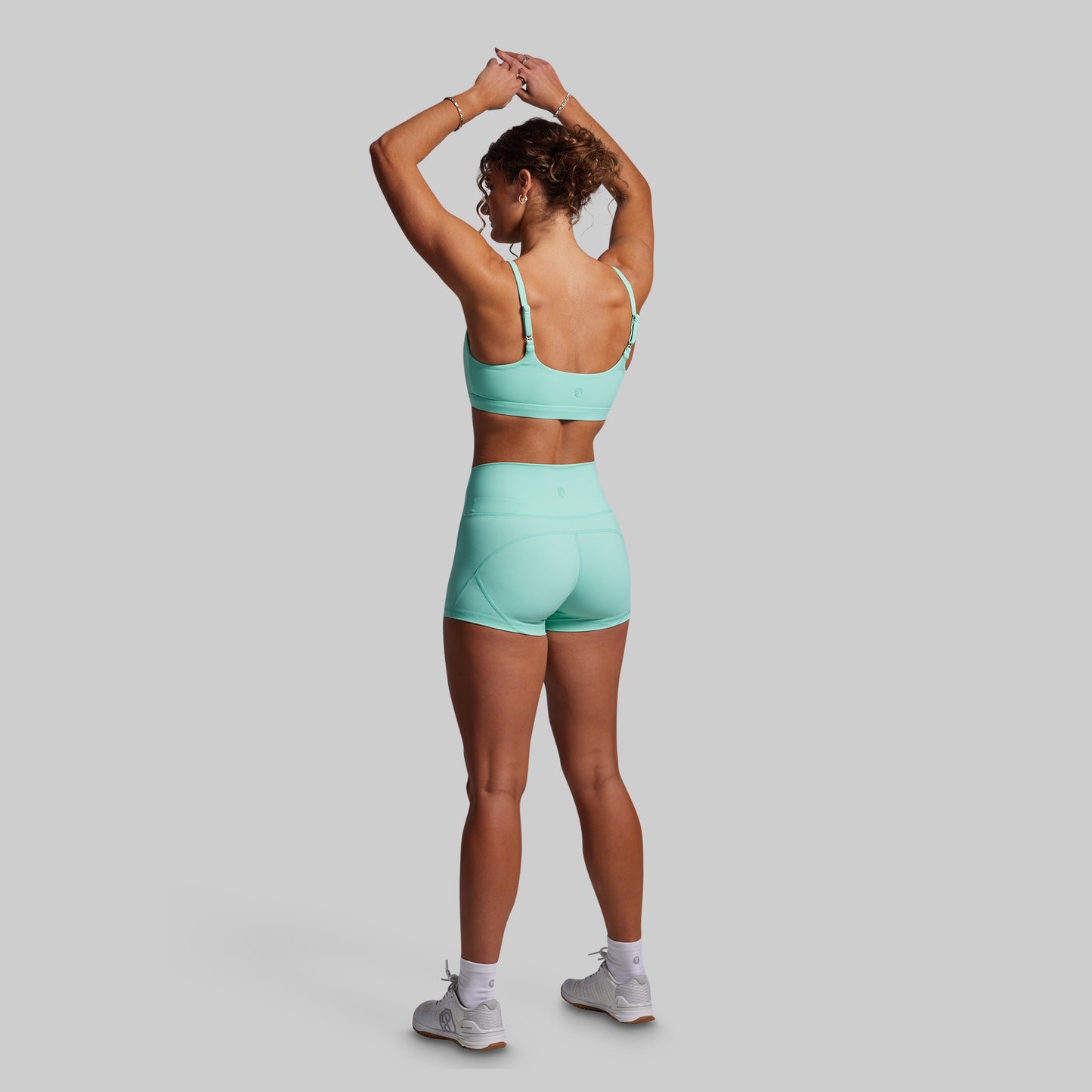 Woman wearing a matching teal sports bra and shorts set on a gray background