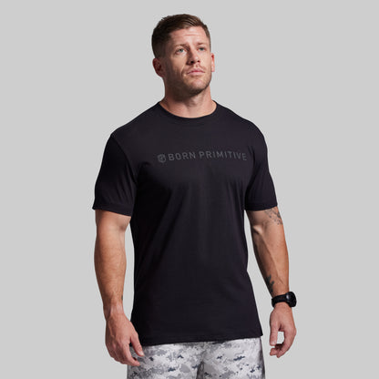 Man wearing a black 'Born Primitive' t-shirt on a gray background