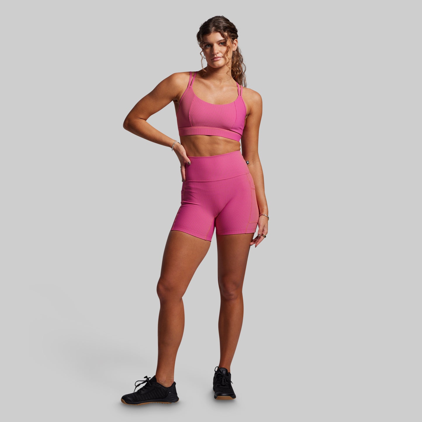Woman wearing a pink ribbed athletic outfit on a gray background