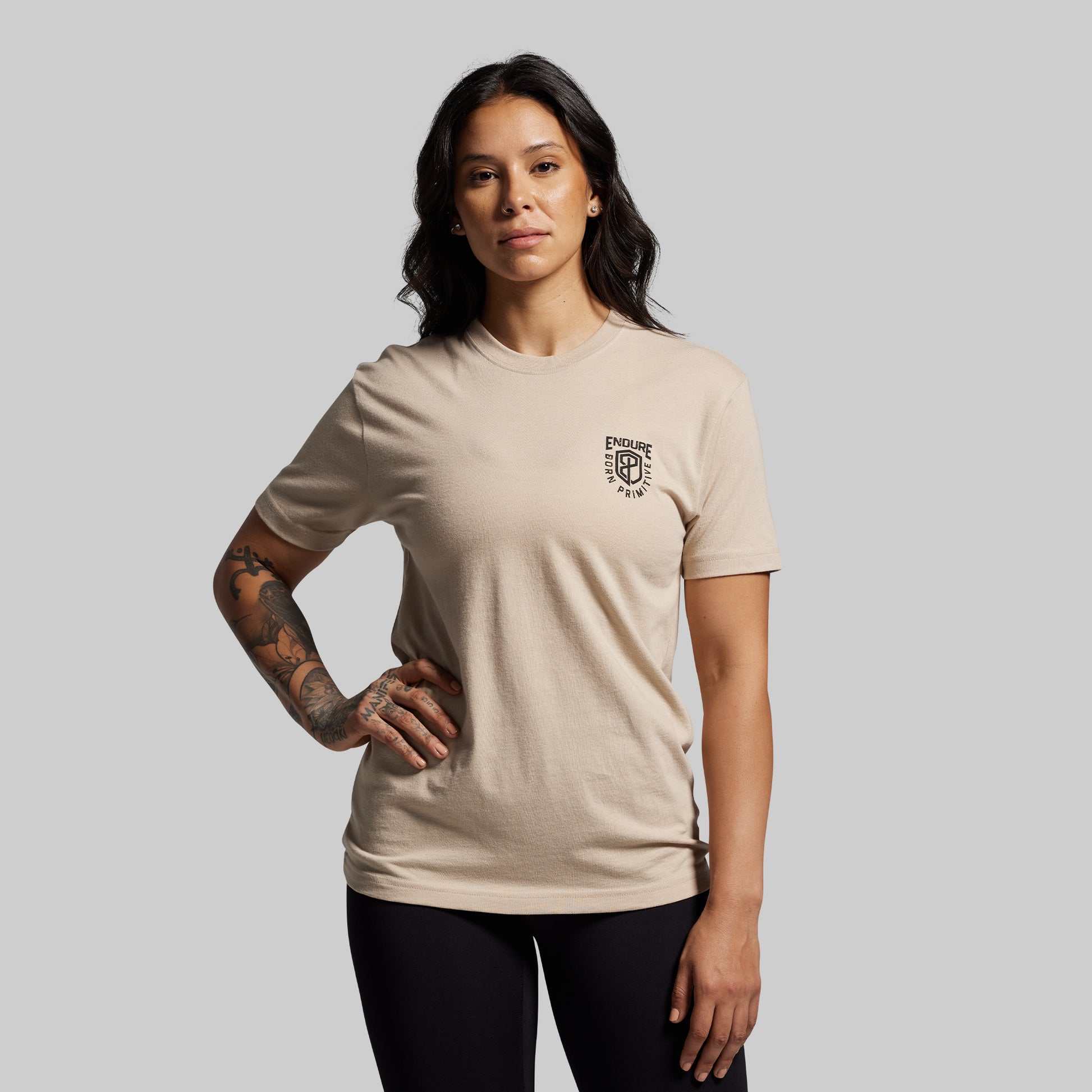 Woman wearing a beige t-shirt with a logo on a gray background