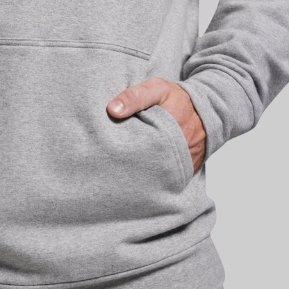 Person wearing a gray hoodie with a hand in the pocket on a light gray background