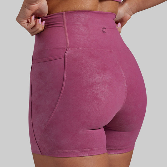 Rear view of a person wearing high-waisted athletic shorts in a dusty rose pink color, showing the pockets and waistband details against a solid gray background.