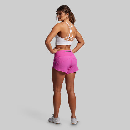 Woman wearing a white sports bra and pink shorts on a gray background