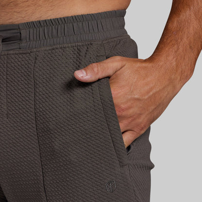Close-up of a person wearing textured dark gray athletic joggers, showing the side pocket with a hand inserted and an elastic waistband.