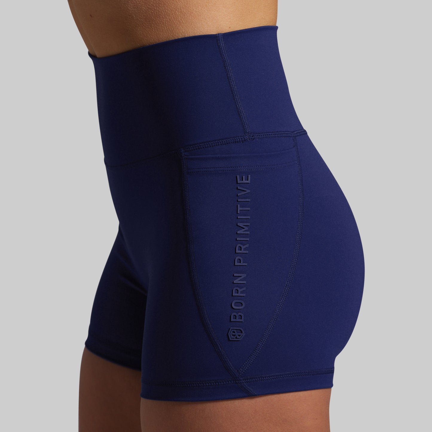 Navy blue athletic shorts with 'Born Primitive' branding on a gray background