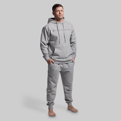 Man wearing a gray hoodie and jogger set with a brand logo on a light gray background