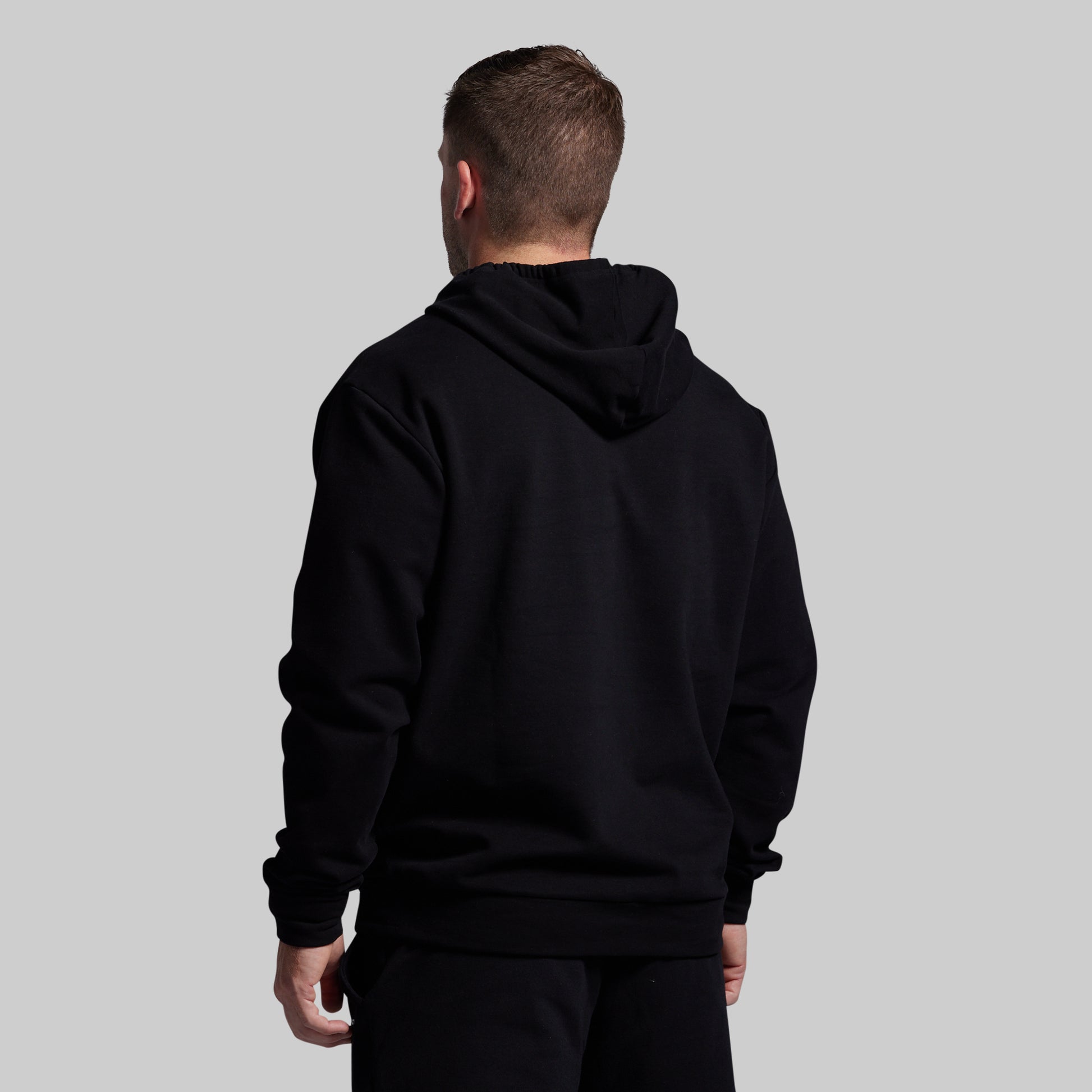 Person wearing a black hoodie from behind on a gray background