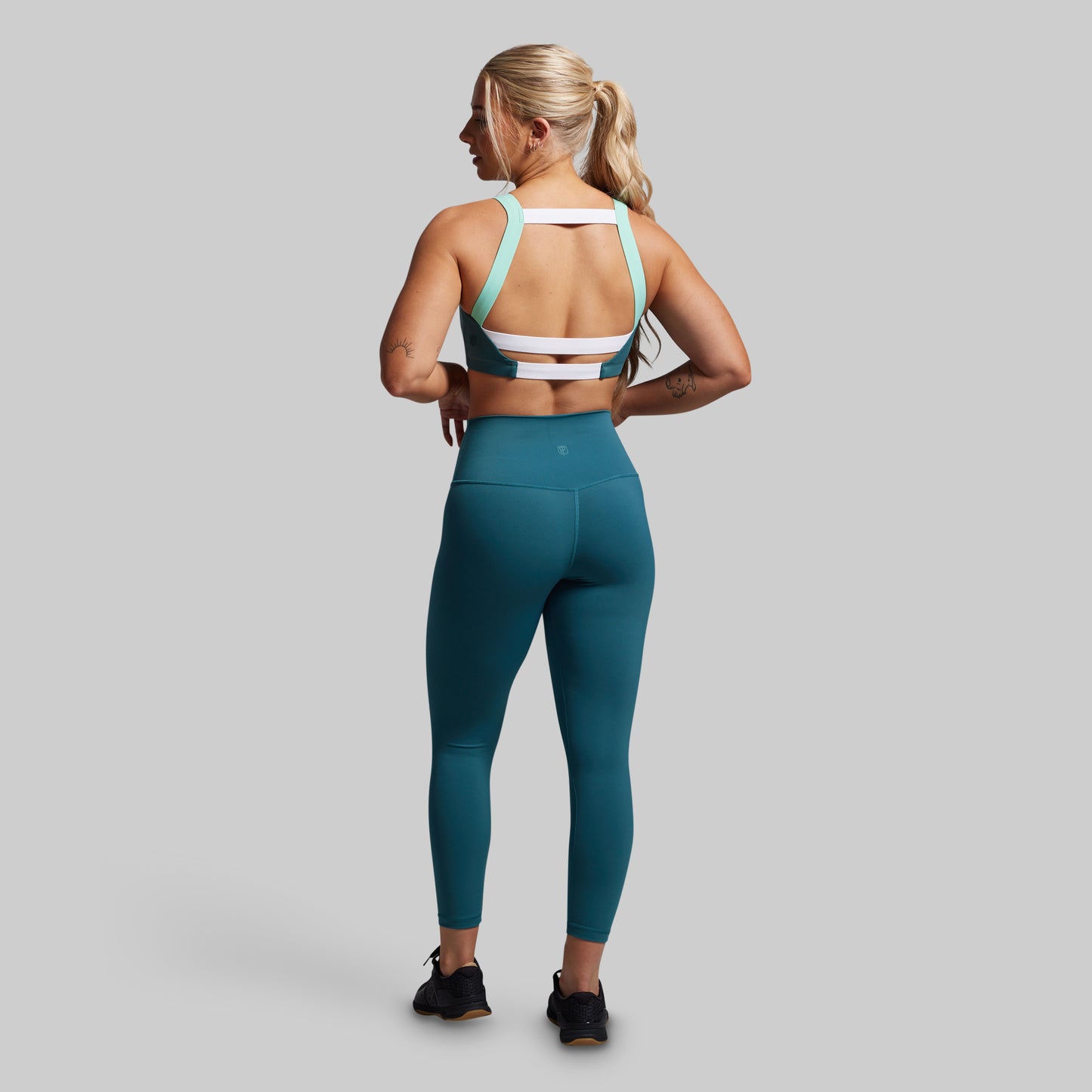 Woman wearing a teal sports bra and leggings set on a gray background