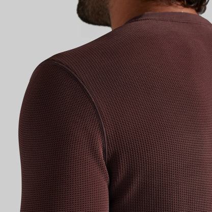 Close-up back view of a person wearing a textured, waffle-knit long-sleeve shirt in a deep burgundy brown color, set against a solid light gray background.