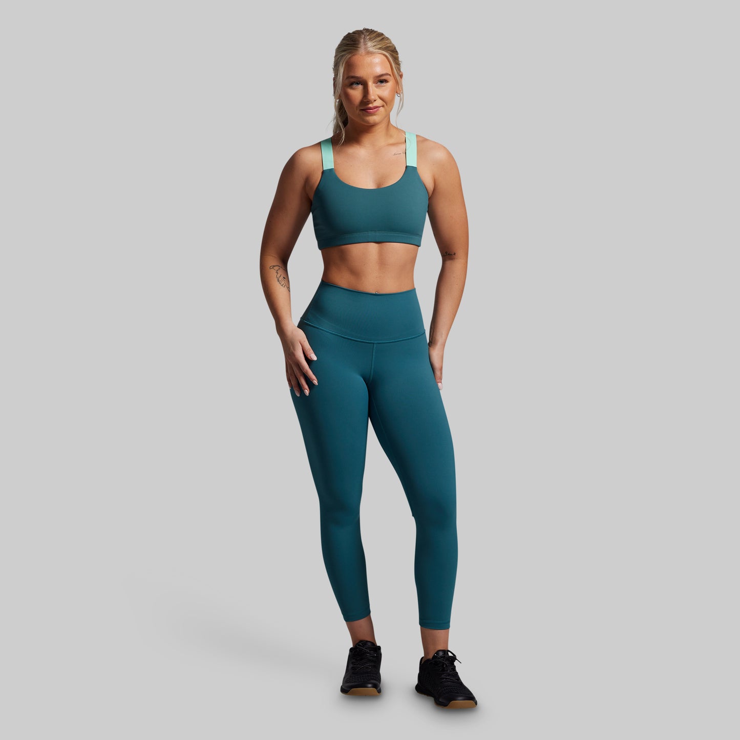 Woman wearing a teal sports bra and leggings set on a gray background