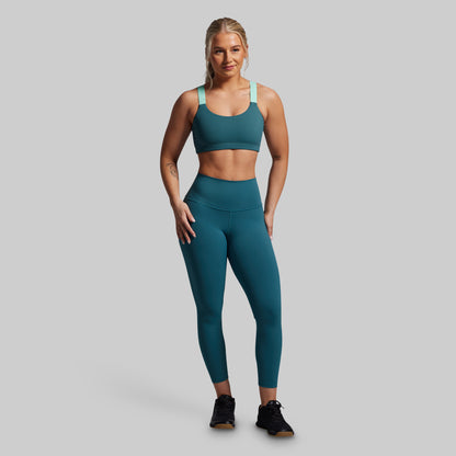 Woman wearing a teal sports bra and leggings set on a gray background