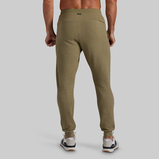 A man wearing textured olive green jogger pants, shown from the back against a solid gray studio background.