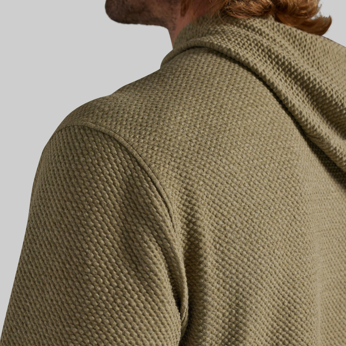 Close-up of a person wearing a textured olive green hooded sweatshirt, showing the back of the neck, shoulder, and the waffle-knit fabric.