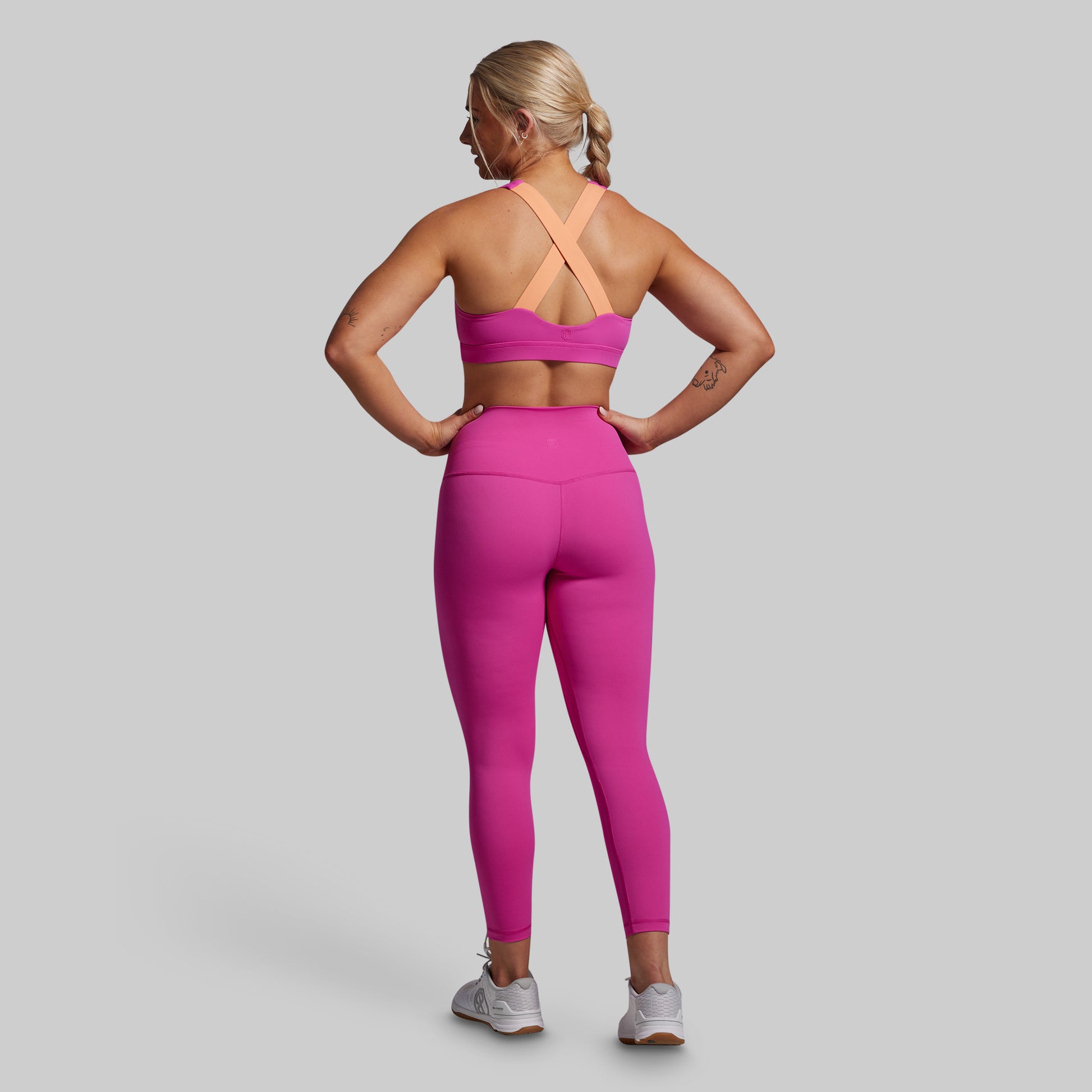 Woman wearing a pink sports bra and leggings set on a gray background