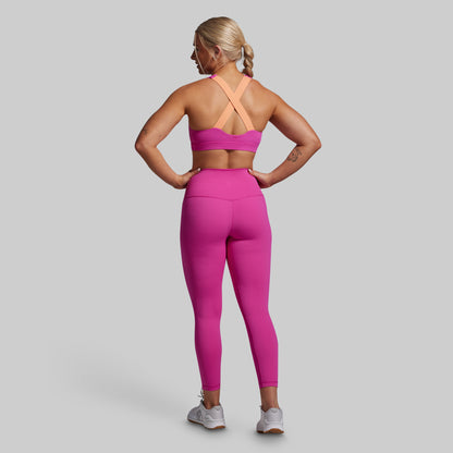 Woman wearing a pink sports bra and leggings set on a gray background