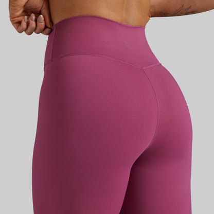Close-up back view of a person wearing high-waisted athletic leggings in a muted berry pink color, showing the waistband and hip area against a plain light gray background.
