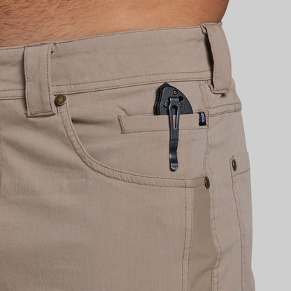 Close-up of khaki pants worn by a person, showing the back pocket with a black clip holding a small black accessory, against a light gray background.