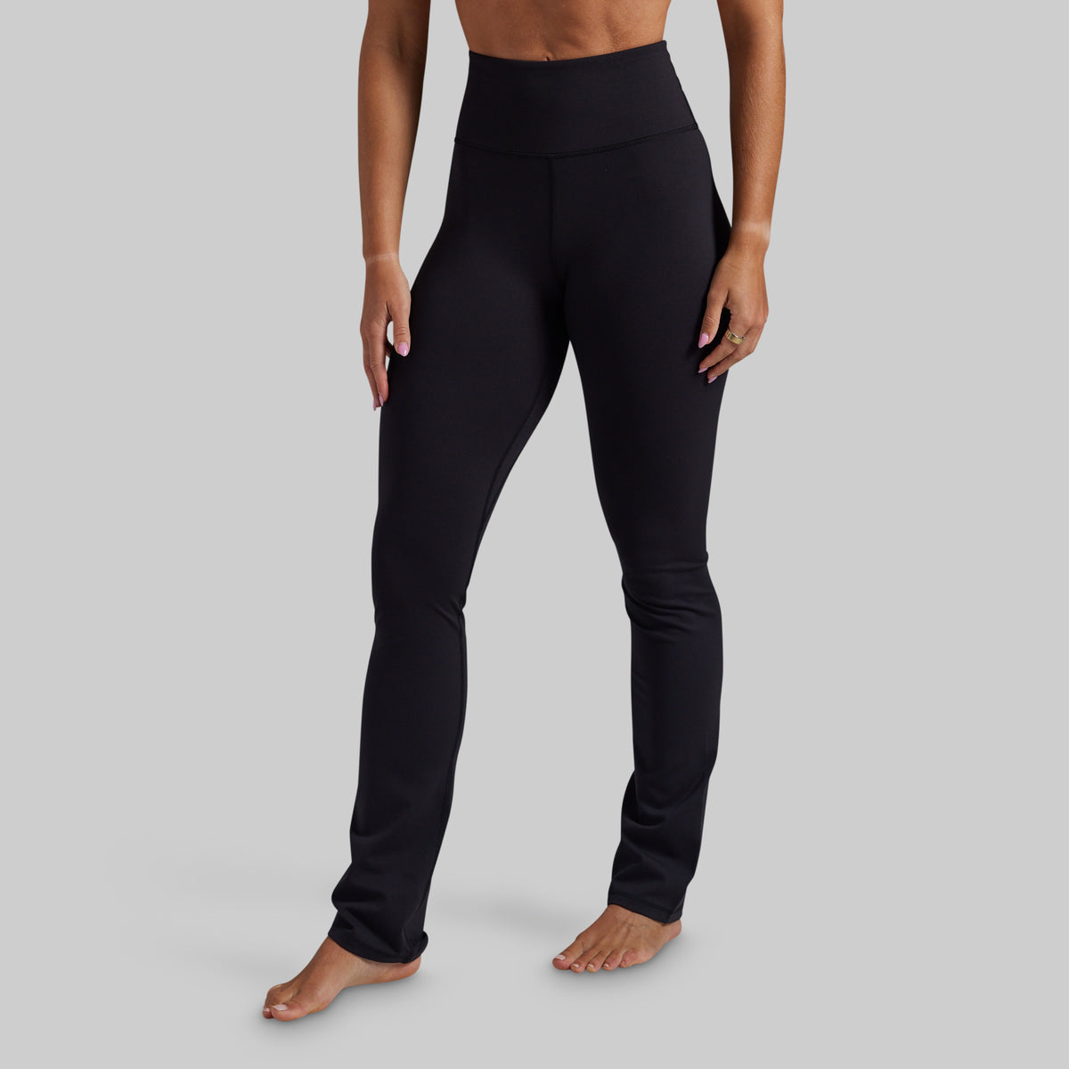 A model wearing black high-waisted yoga pants, shown from the waist down against a solid gray background.