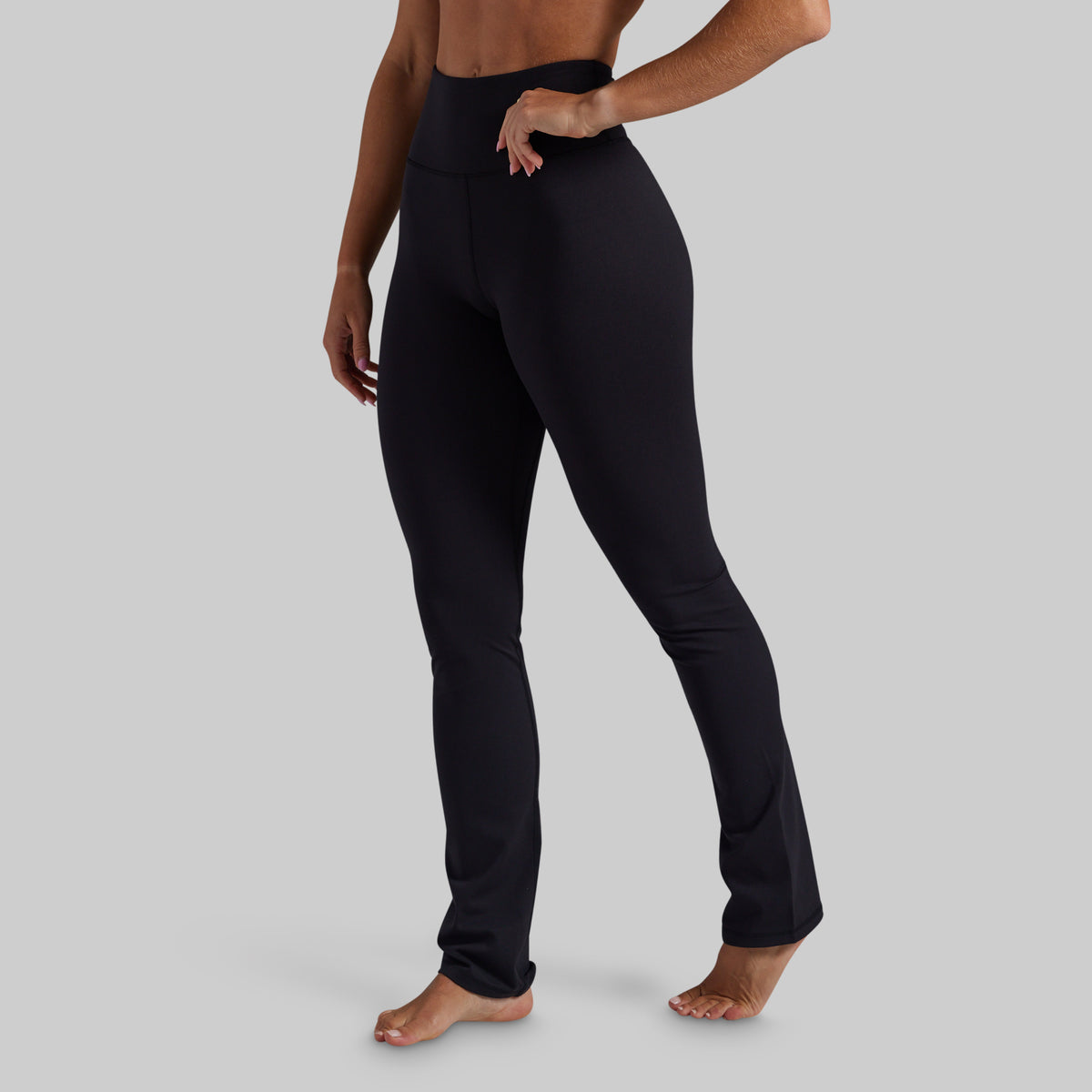 A model wearing black high-waisted yoga pants, shown from the waist down against a solid gray background.