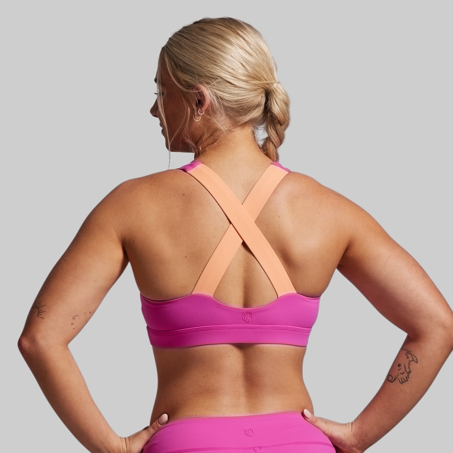 Woman wearing a pink sports bra and leggings on a gray background