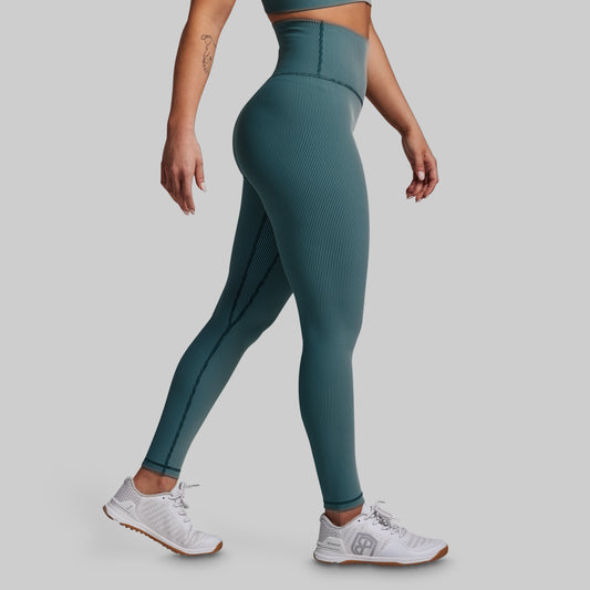 Person wearing teal ribbed leggings and white sneakers on a gray background