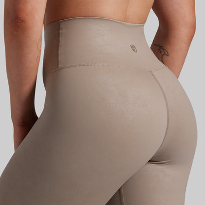 Close-up rear view of a person wearing high-waisted taupe leggings against a light gray studio background.
