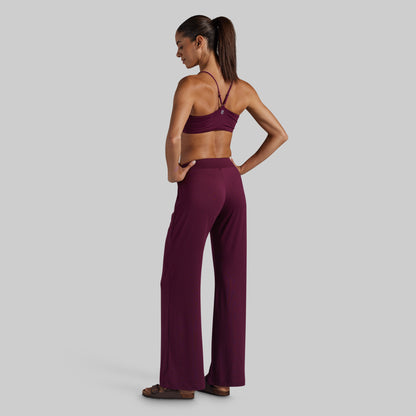 A woman stands in profile wearing a matching burgundy lounge set consisting of a lounge bra and high-waisted wide-leg pants.