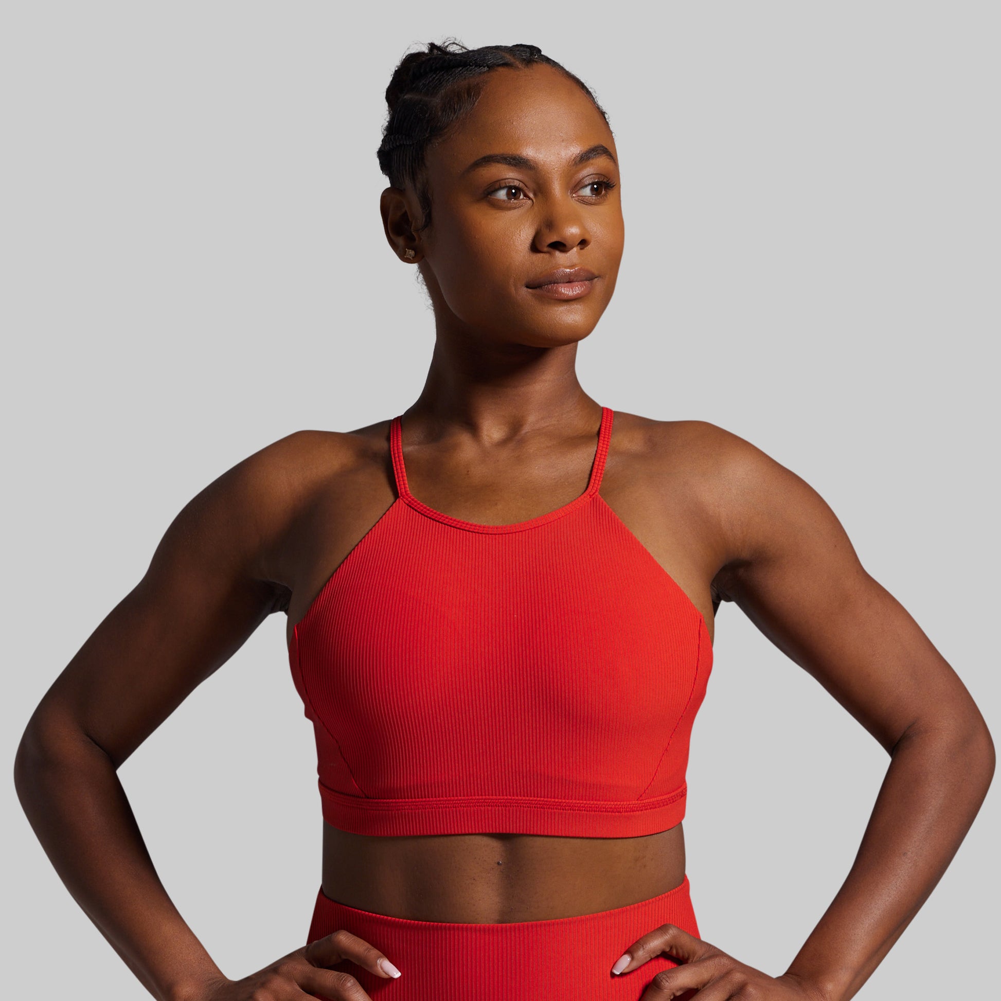 Woman wearing a red sports bra and shorts on a gray background
