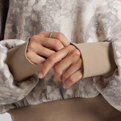 Close-up of a model wearing a beige sweater with a gray and beige abstract floral patterned outer layer.