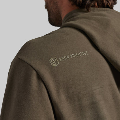 Close-up of a person wearing an olive brown hooded sweatshirt, showing the back of the neck, shoulder, and upper back. The brand name 'BORN PRIMITIVE' with its geometric logo is printed in tonal olive on the upper left shoulder.