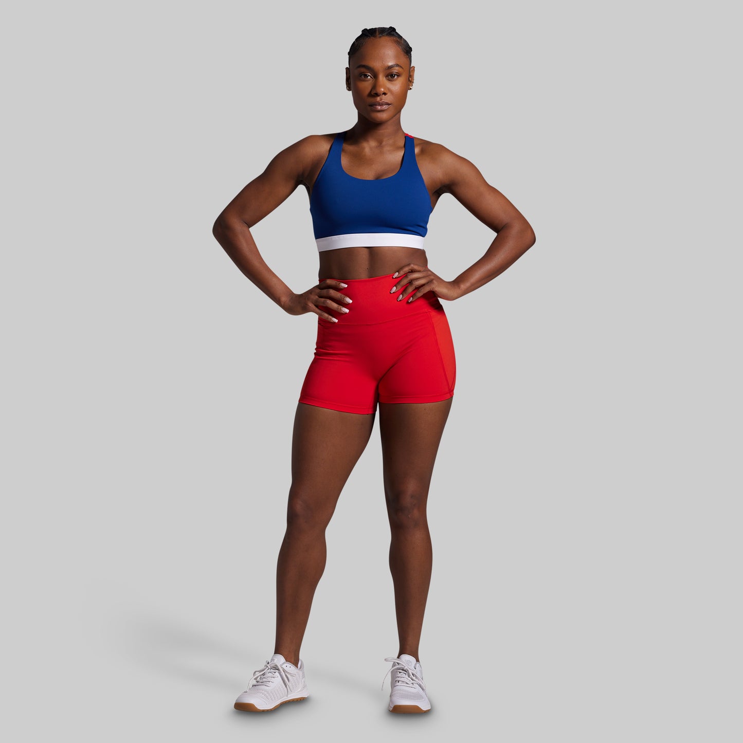 Woman wearing a blue sports bra and red shorts on a gray background
