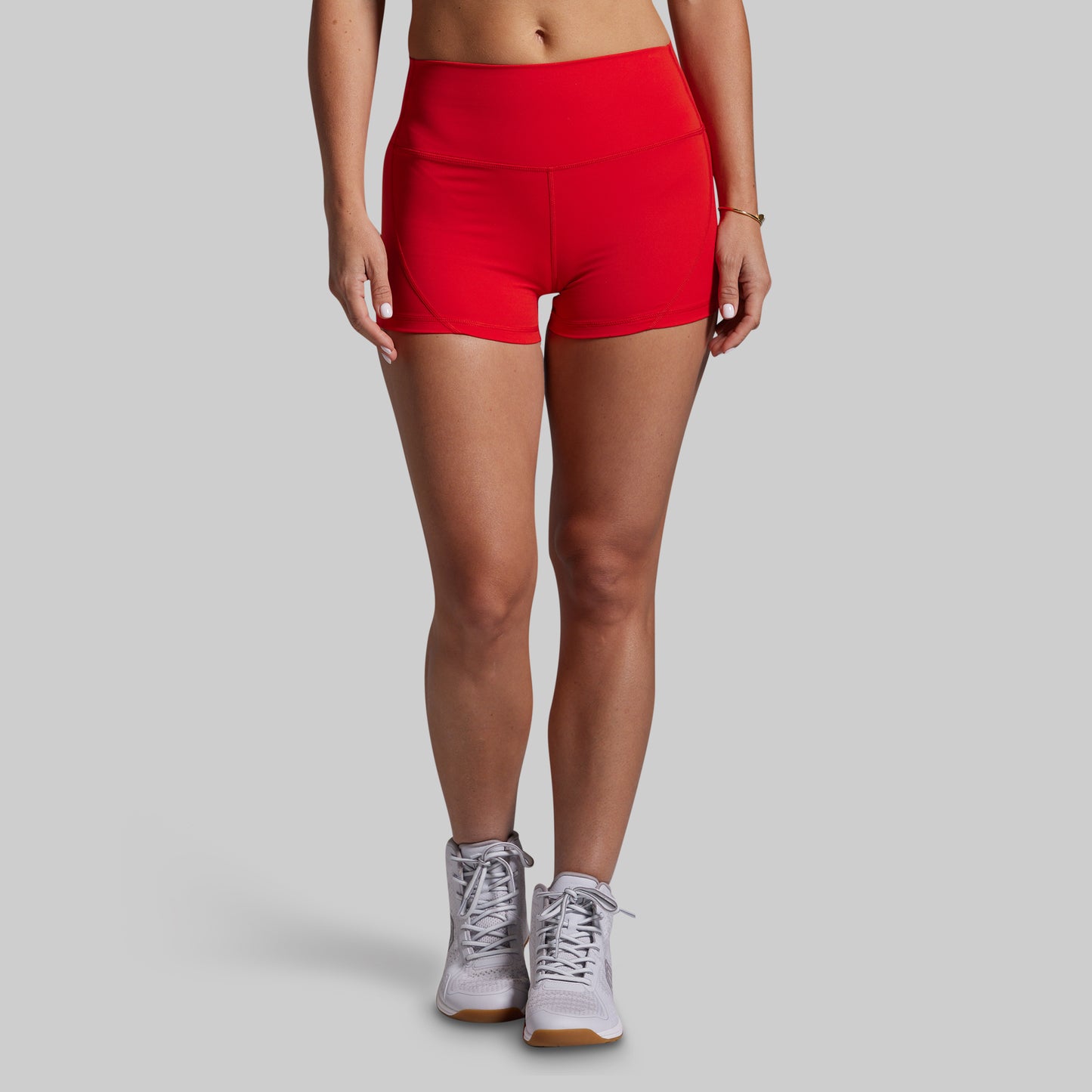 Person wearing red athletic shorts and white sneakers on a gray background