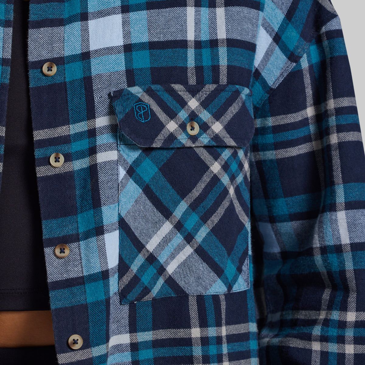 Close-up of a blue and navy plaid flannel shirt with a chest pocket and snap-button flap, worn over a dark undershirt.