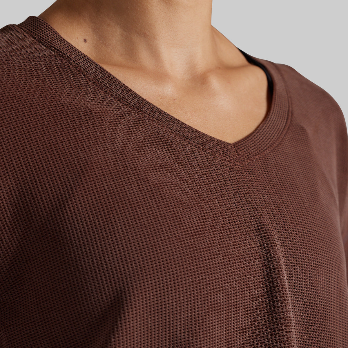 Close-up of a person wearing a brown textured V-neck top against a light gray background.