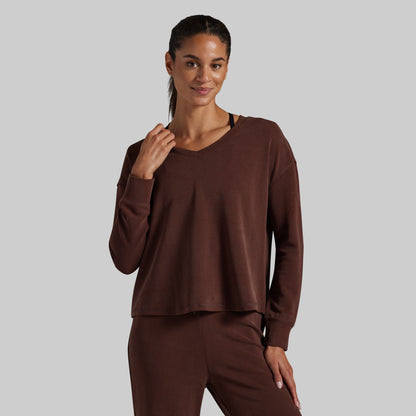 A woman modeling a matching brown lounge set consisting of a long-sleeve cropped V-neck top and coordinating pants, photographed against a solid light gray background.