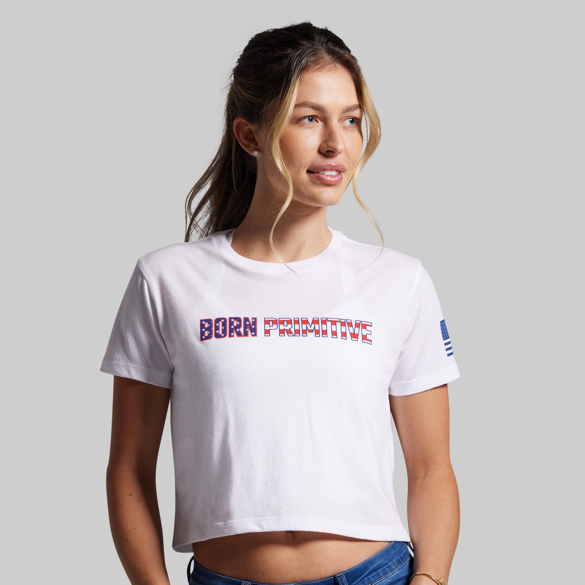 Woman wearing a white t-shirt with 'Born Primitive' text on a plain background